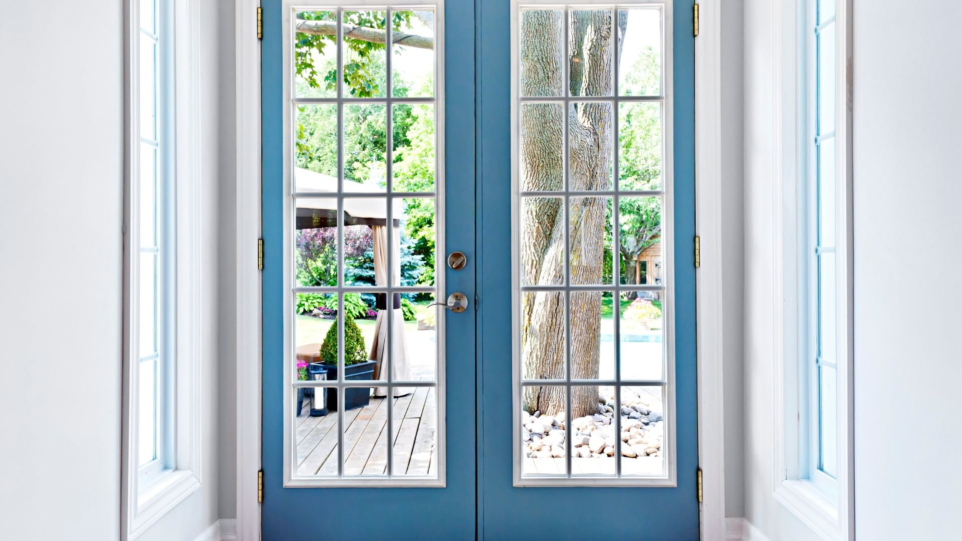 Blue French doors open to wooden deck with trees and garden view